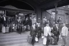 Schwarz-Weiß-Foto, das viele Männer zeigt, die mit ihren Koffern aus dem Harburger Bahnhof treten. Es vermittelt eine hoffnungsfrohe Stimmung.